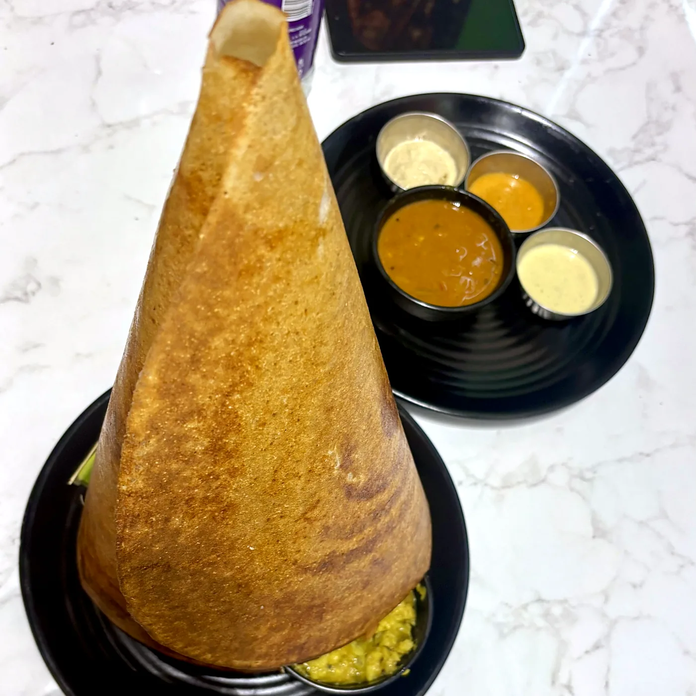 A tall cone of ghee roast dosa with sambar and chutneys