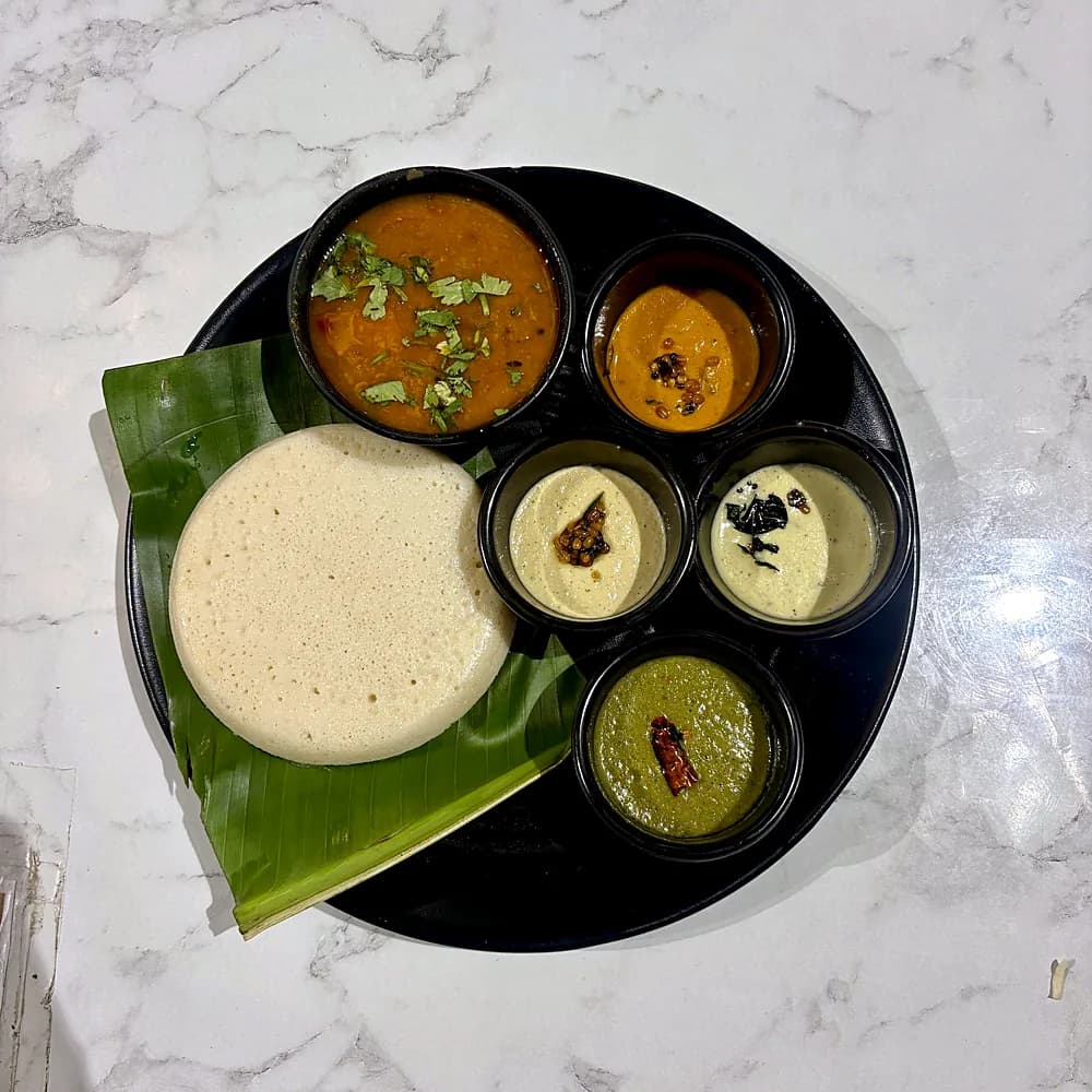 Thatte idli with sambar and chutneys on a banana leaf